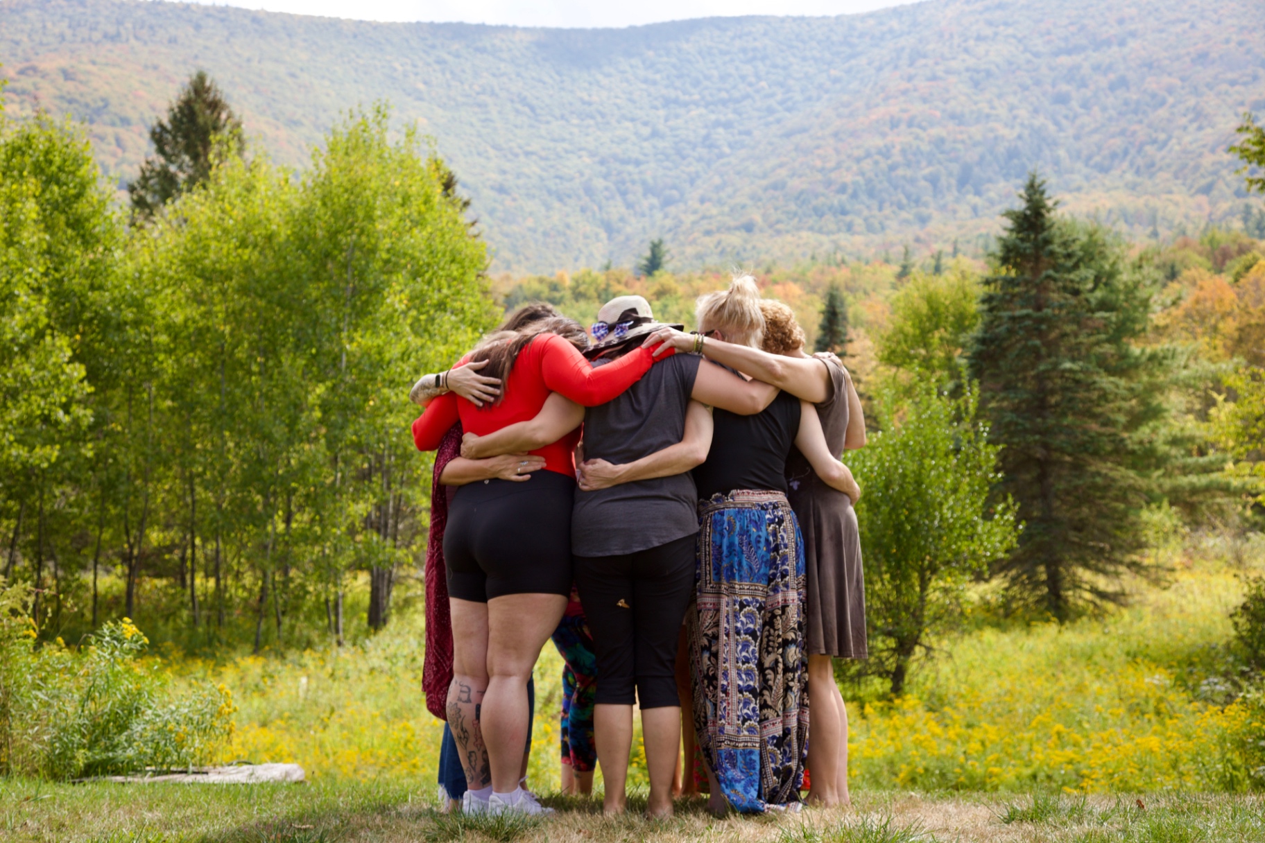 A circle of women embracing in a mountain meadow during a Held Sacred retreat