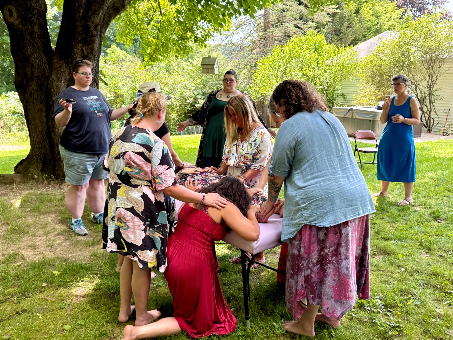 A circle of women giving a group healing under a tree in the garden