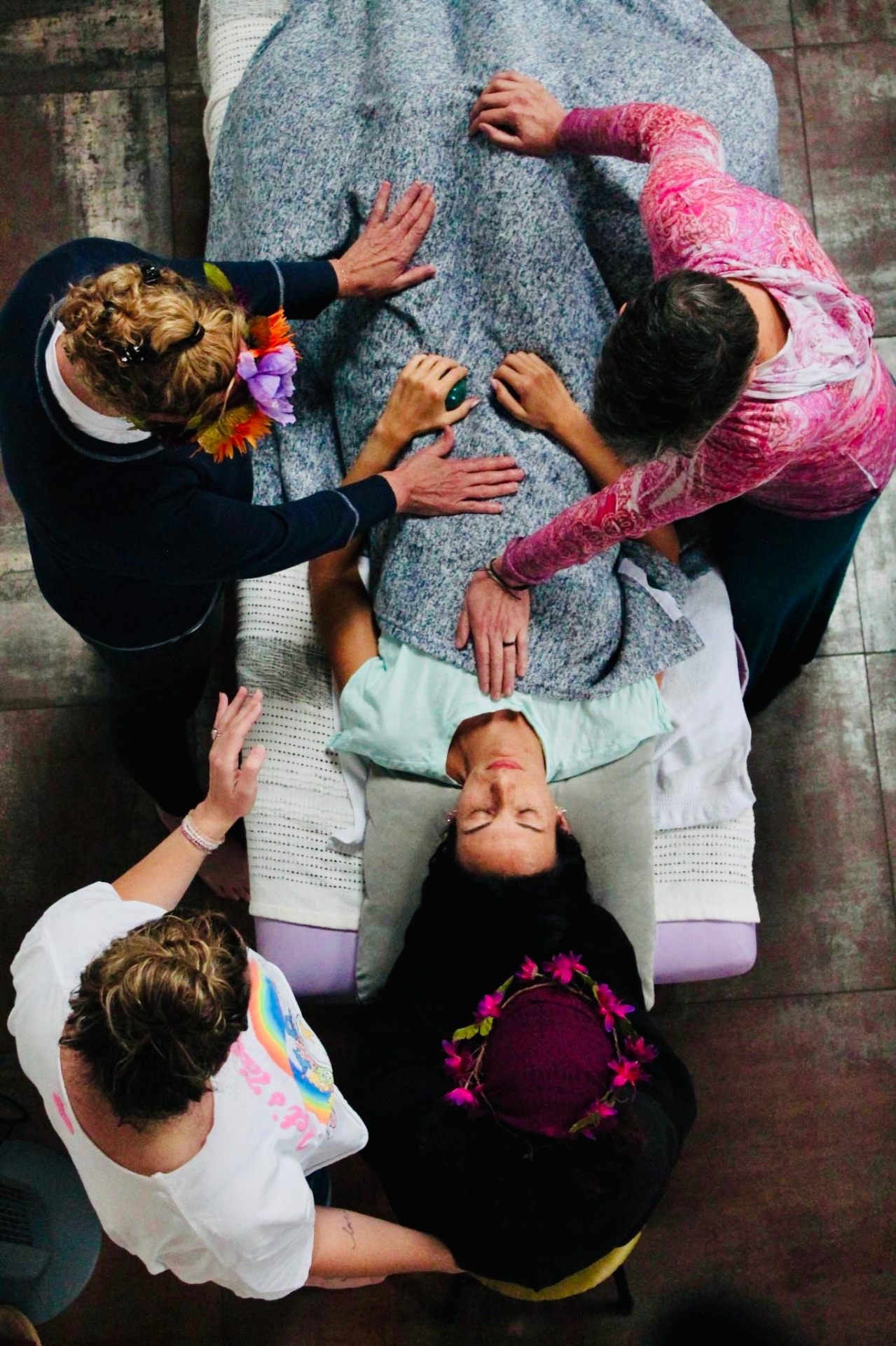 Overhead view of a woman receiving hands-on healing from a circle of Held Sacred sisters